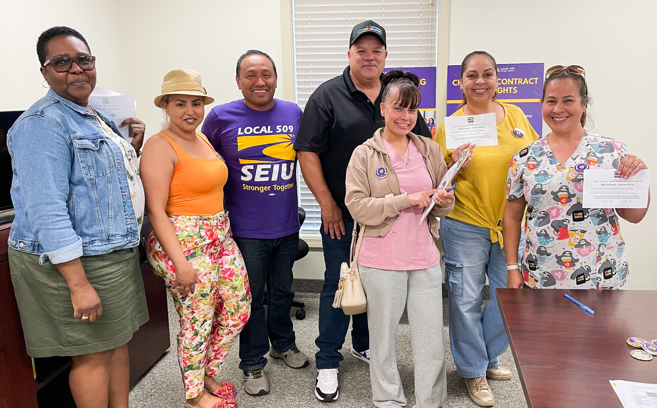A group of seven people, some holding papers, stand together smiling in an office with SEIU Local 509 union posters visible on the wall behind them.