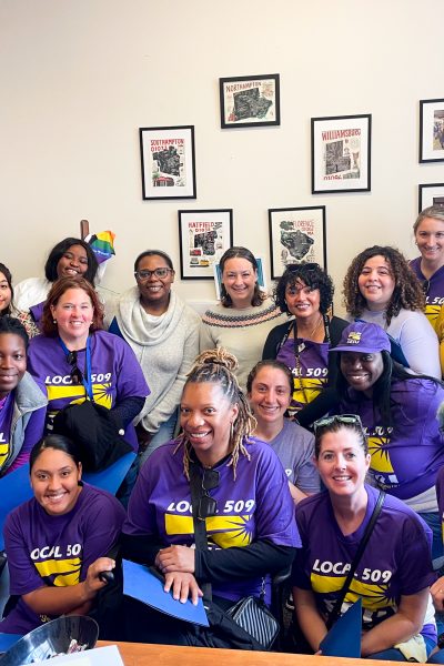 A group of people, many wearing matching purple “Local 509” shirts, pose and smile together indoors in a room with framed photos and maps on the wall behind them.